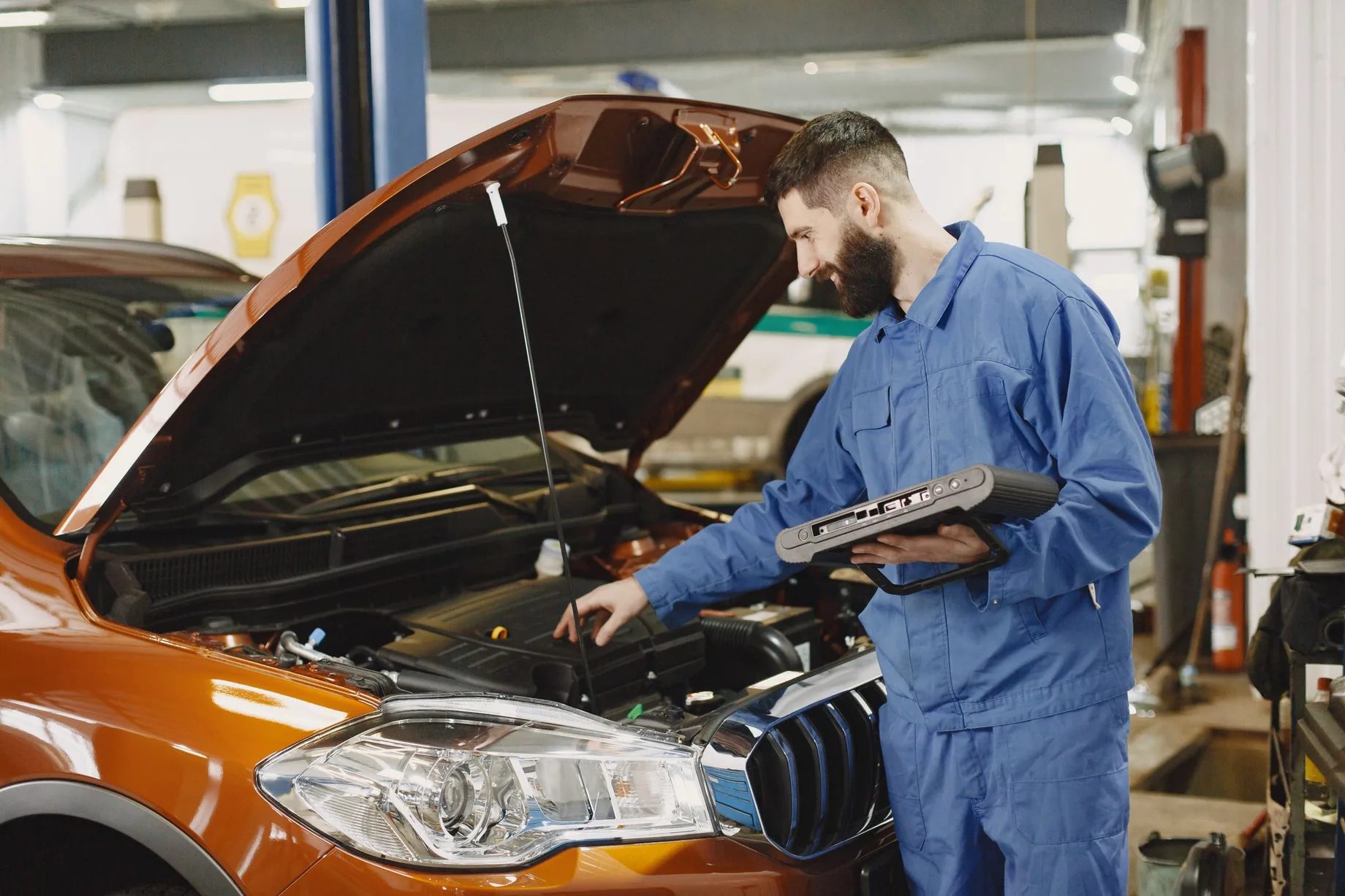 Mechaniker prüft einen geöffneten Motorraum in einer Werkstatt; illustratives Stockfoto.